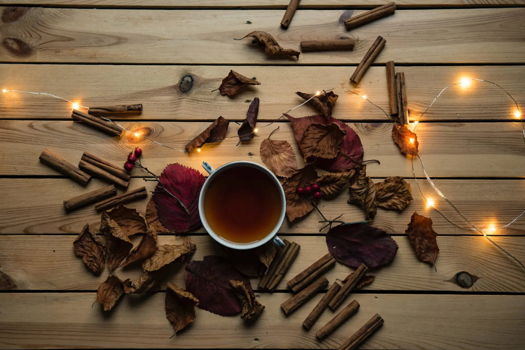Taza de té de hierbas caliente rodeada de hojas otoñales.